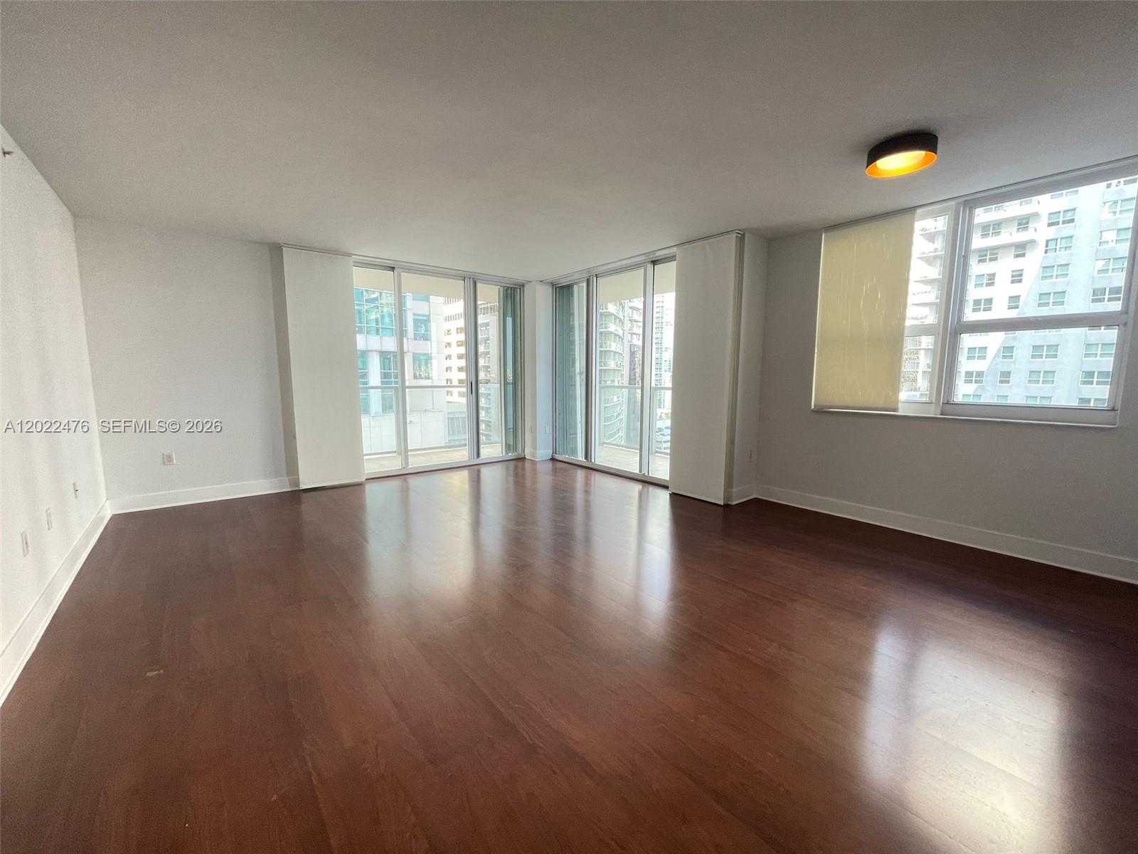 An empty room features dark wood flooring, white walls, and floor-to-ceiling windows — 1155 Brickell Bay Dr # 1102, Miami FL 33131, MIAMI, FL