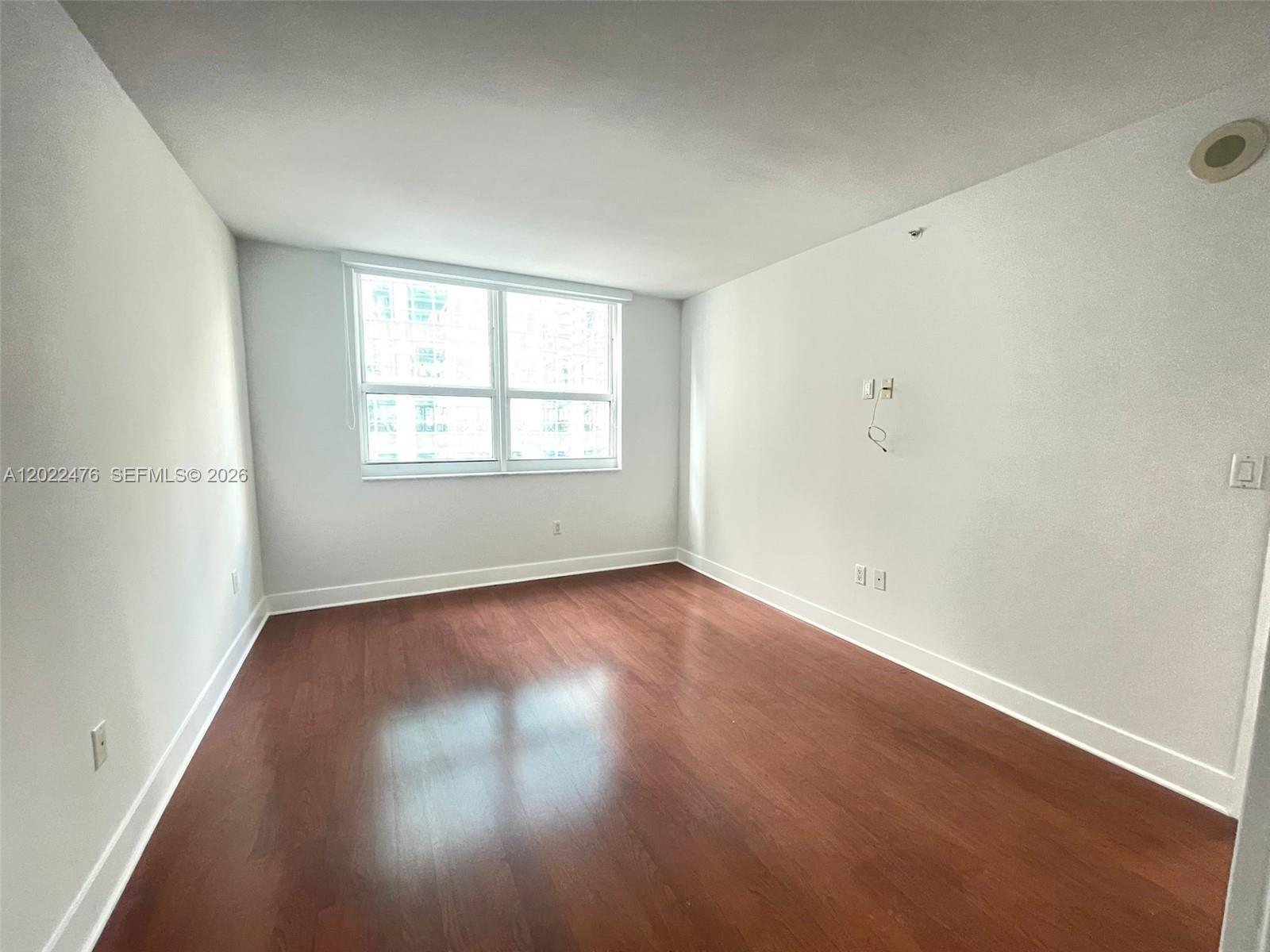 An empty room features white walls, dark wood-look flooring, and a large window — 1155 Brickell Bay Dr # 1102, Miami FL 33131, MIAMI, FL