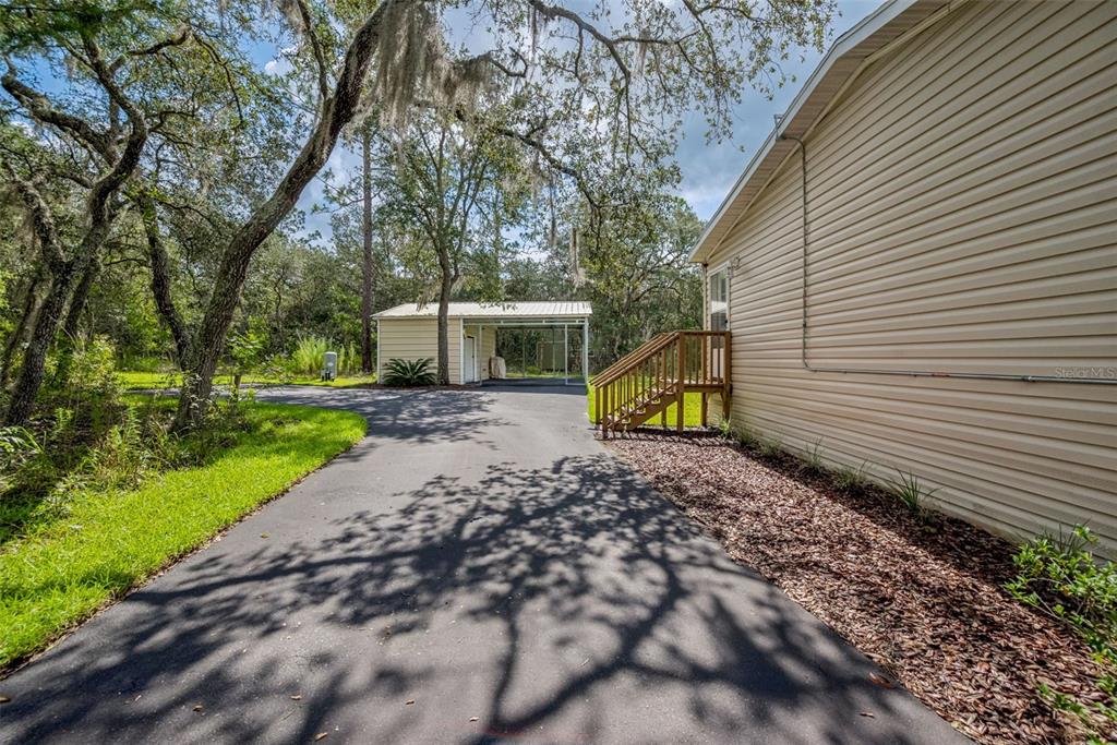 A paved driveway leads to a detached carport next to a house with tan siding — 8261 NE 118TH TERRACE, BRONSON, FL