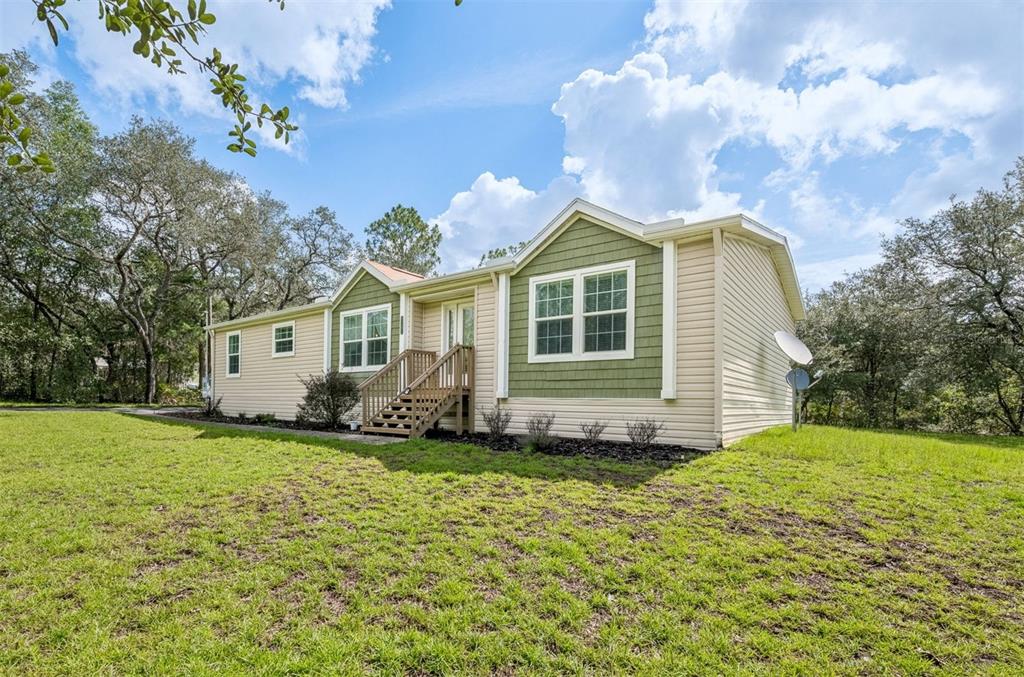 A single-story house with beige siding, green shingle accents, and wooden front steps — 8261 NE 118TH TERRACE, BRONSON, FL