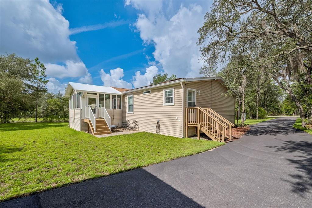 A beige mobile home with a screened porch, wooden stairs, and an asphalt driveway — 8261 NE 118TH TERRACE, BRONSON, FL