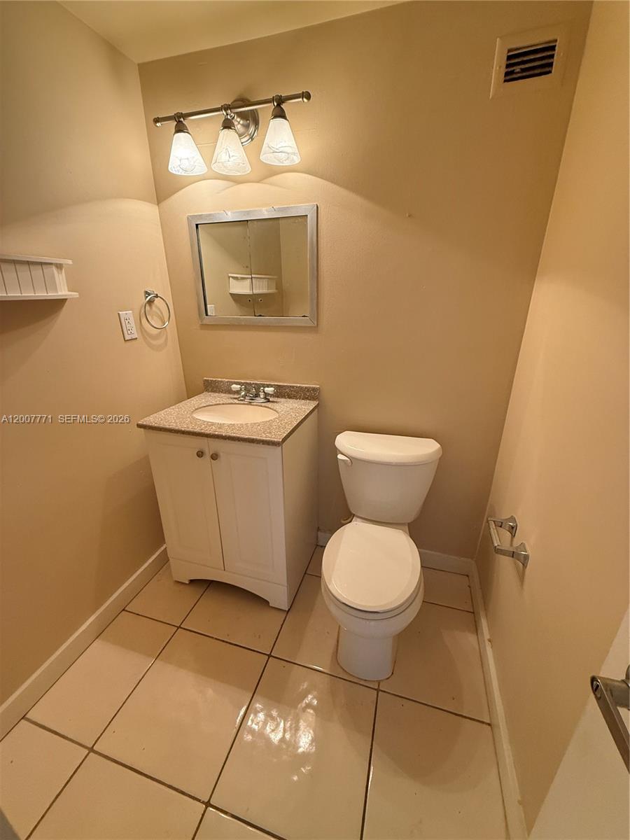 A small bathroom features a white vanity, a mirror, and a toilet on tiled floors — 5313 Collins Ave # 906, Miami Beach FL 33140, MIAMI BEACH, FL