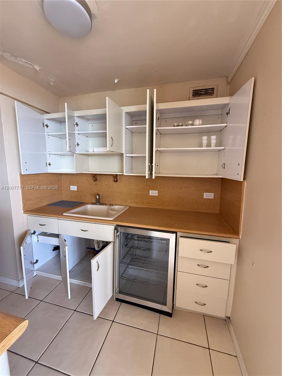 A small kitchen features white cabinets, a light-colored countertop, and a built-in wine cooler — 5313 Collins Ave # 906, Miami Beach FL 33140, MIAMI BEACH, FL