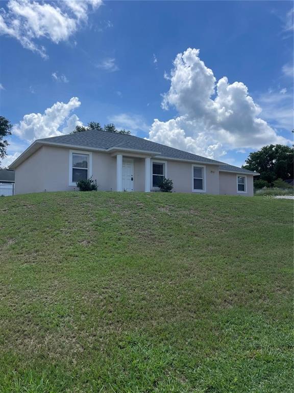 A light-colored, single-story house with a gray shingled roof sits atop a grassy hill — 17542 DORIS STREET, MONTVERDE, FL