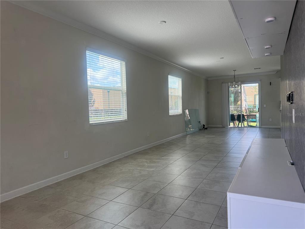 An empty living area features light-colored tile flooring, two windows, and sliding glass patio doors — 4724 TRIBUTE TRAIL, KISSIMMEE, FL