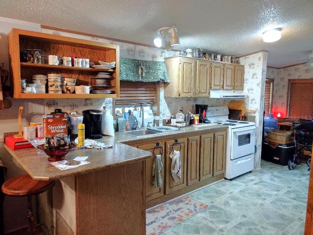 A kitchen features wood cabinets, laminate countertops, a white stove, and a breakfast bar — 1176 COUNTY ROAD 305, BUNNELL, FL