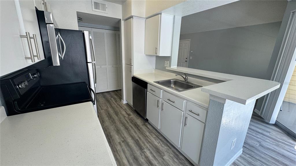 A kitchen features white cabinets, stainless steel appliances, and a breakfast bar overlooking the living area — 1037 S HIAWASSEE ROAD UNIT 2833, ORLANDO, FL