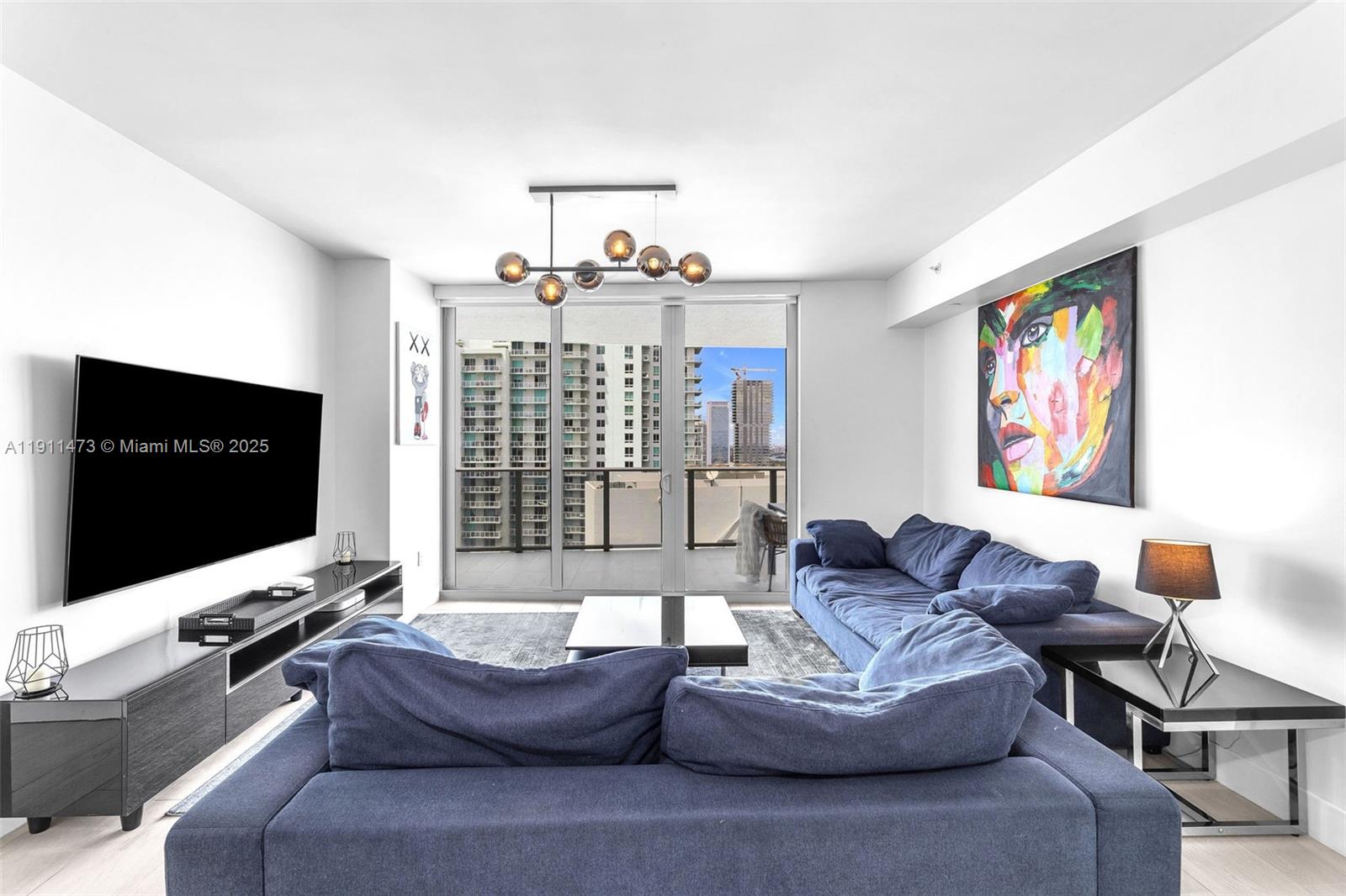 A modern living room features a blue sectional sofa, a large television, and balcony views — 488 NE 18th St # 4311, Miami FL 33132, MIAMI, FL