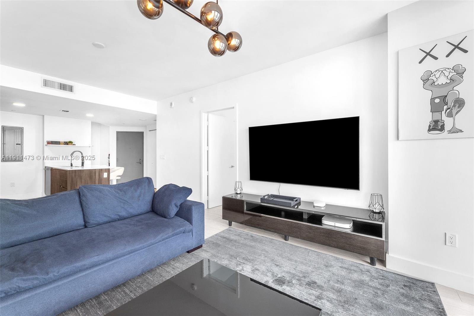 A living room features a blue sofa, a wall-mounted television, and a modern media console — 488 NE 18th St # 4311, Miami FL 33132, MIAMI, FL