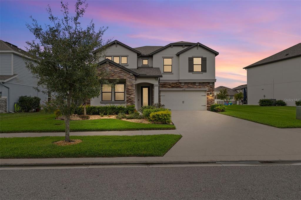 A two-story suburban house features a stone facade, a two-car garage, and a manicured lawn — 31046 PARROT REEF COURT, WESLEY CHAPEL, FL