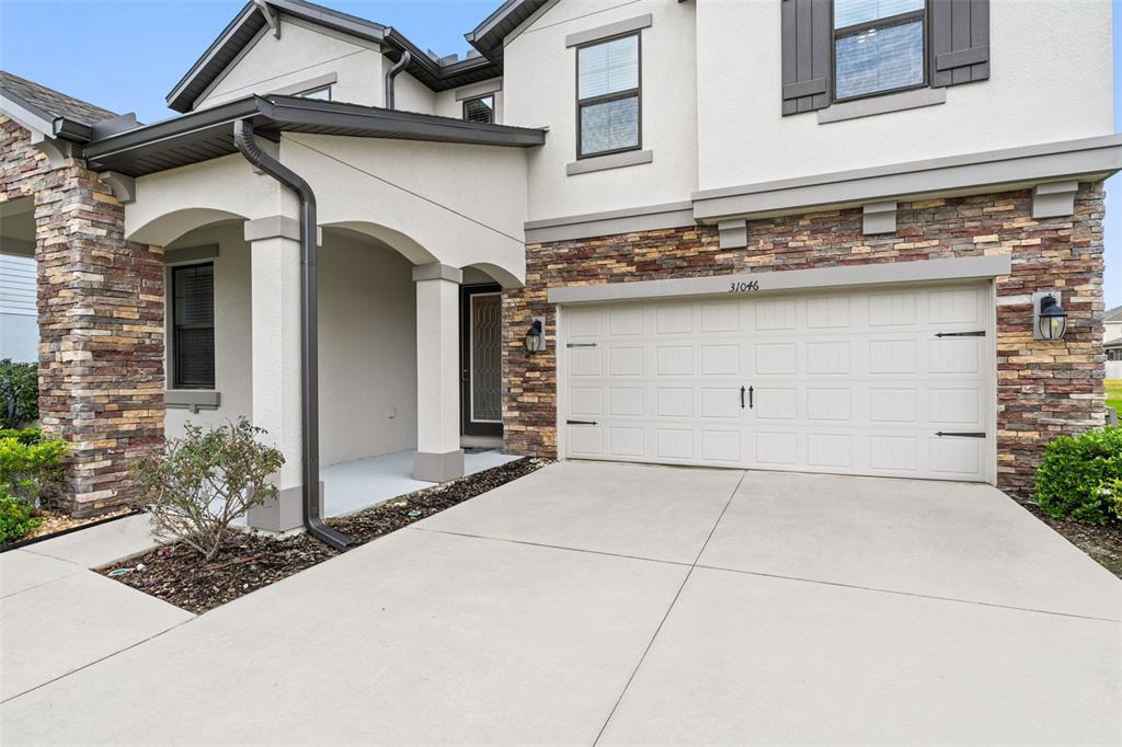 A two-story house exterior features a stone facade, a beige garage door, and a covered entryway — 31046 PARROT REEF COURT, WESLEY CHAPEL, FL