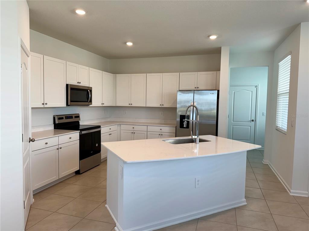 A kitchen features white cabinets, stainless steel appliances, a center island, and tile flooring — 268 REDBUD ROAD, PALM COAST, FL