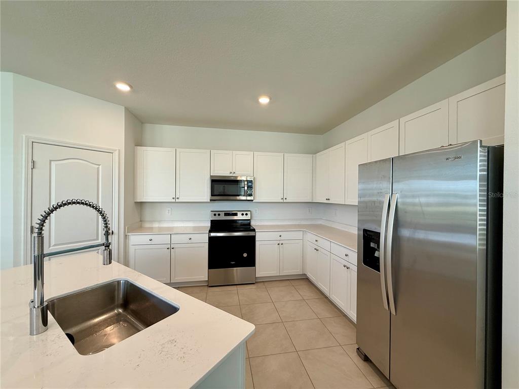 A kitchen features white cabinets, stainless steel appliances, a kitchen island, and tile flooring — 268 REDBUD ROAD, PALM COAST, FL