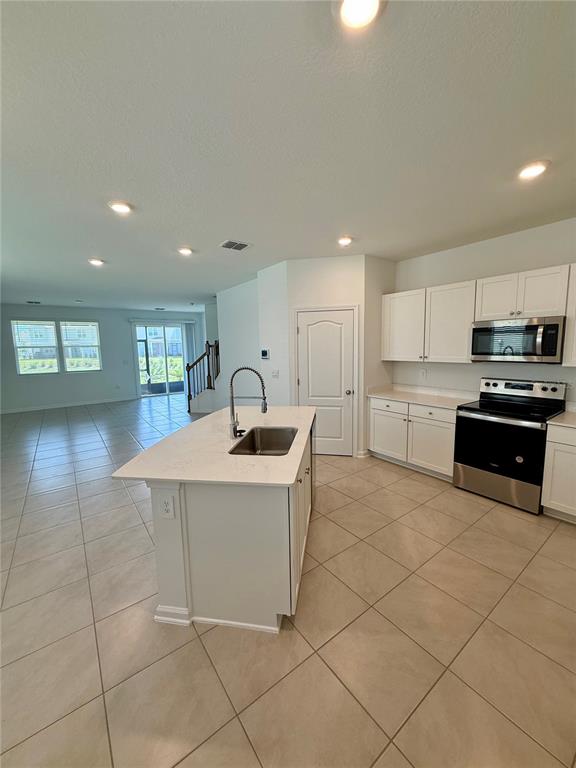 A kitchen features a central island with a sink, white cabinetry, and stainless steel appliances — 268 REDBUD ROAD, PALM COAST, FL