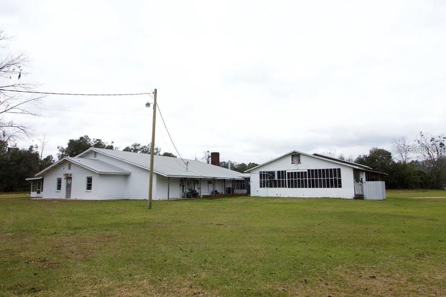A white, single-story building with a metal roof sits on a large, grassy lot — 1606 SW 4TH PLACE, CHIEFLAND, FL