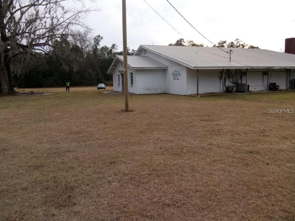 A white, single-story building with a metal roof sits on a large, grassy lot — 1606 SW 4TH PLACE, CHIEFLAND, FL