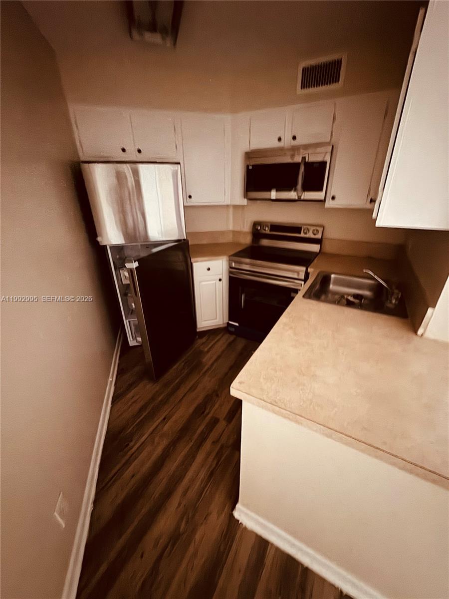 A galley-style kitchen features white cabinets, stainless steel appliances, and wood-look flooring — 211 Lake Pointe Dr # 110, Oakland Park FL 33309, OAKLAND PARK, FL