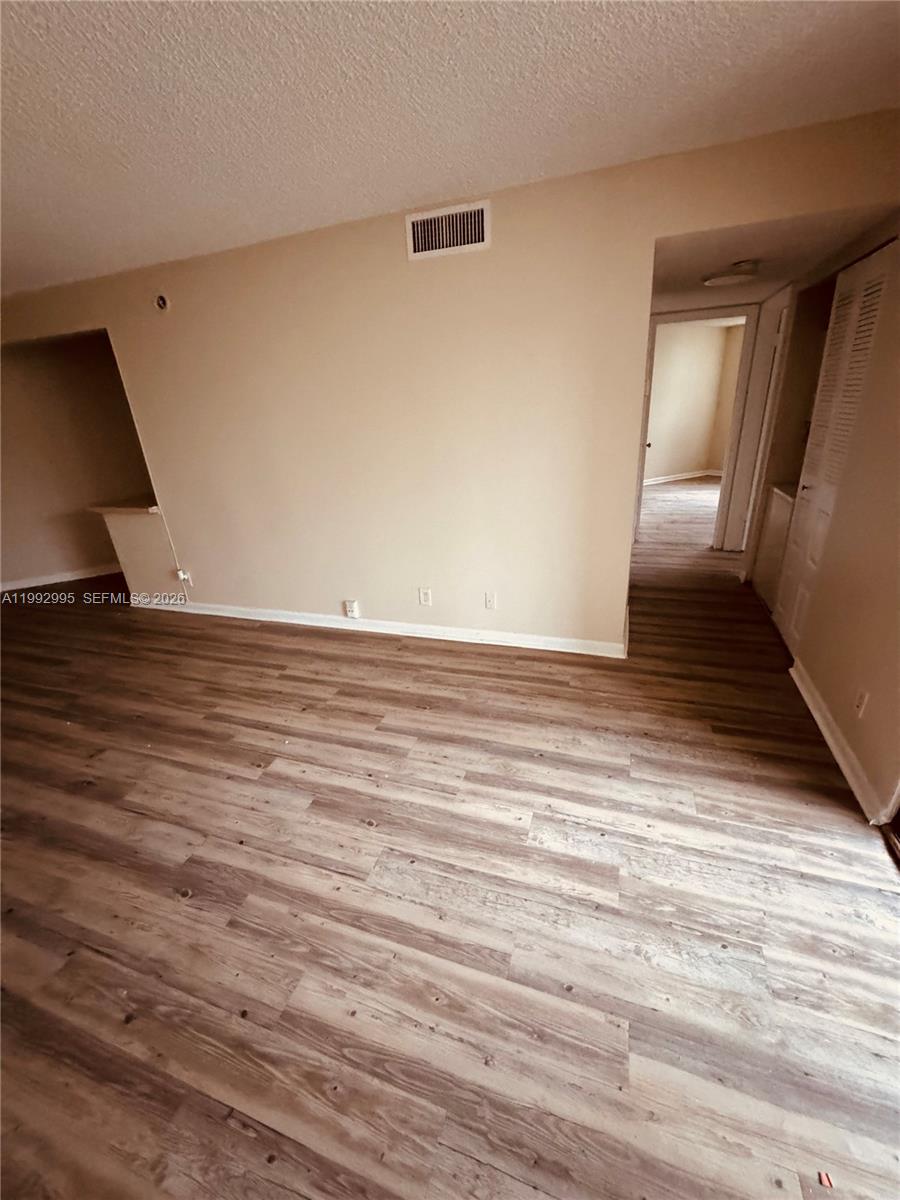 An empty room features light-colored walls, wood-look flooring, and a doorway leading to another area — 211 Lake Pointe Dr # 110, Oakland Park FL 33309, OAKLAND PARK, FL