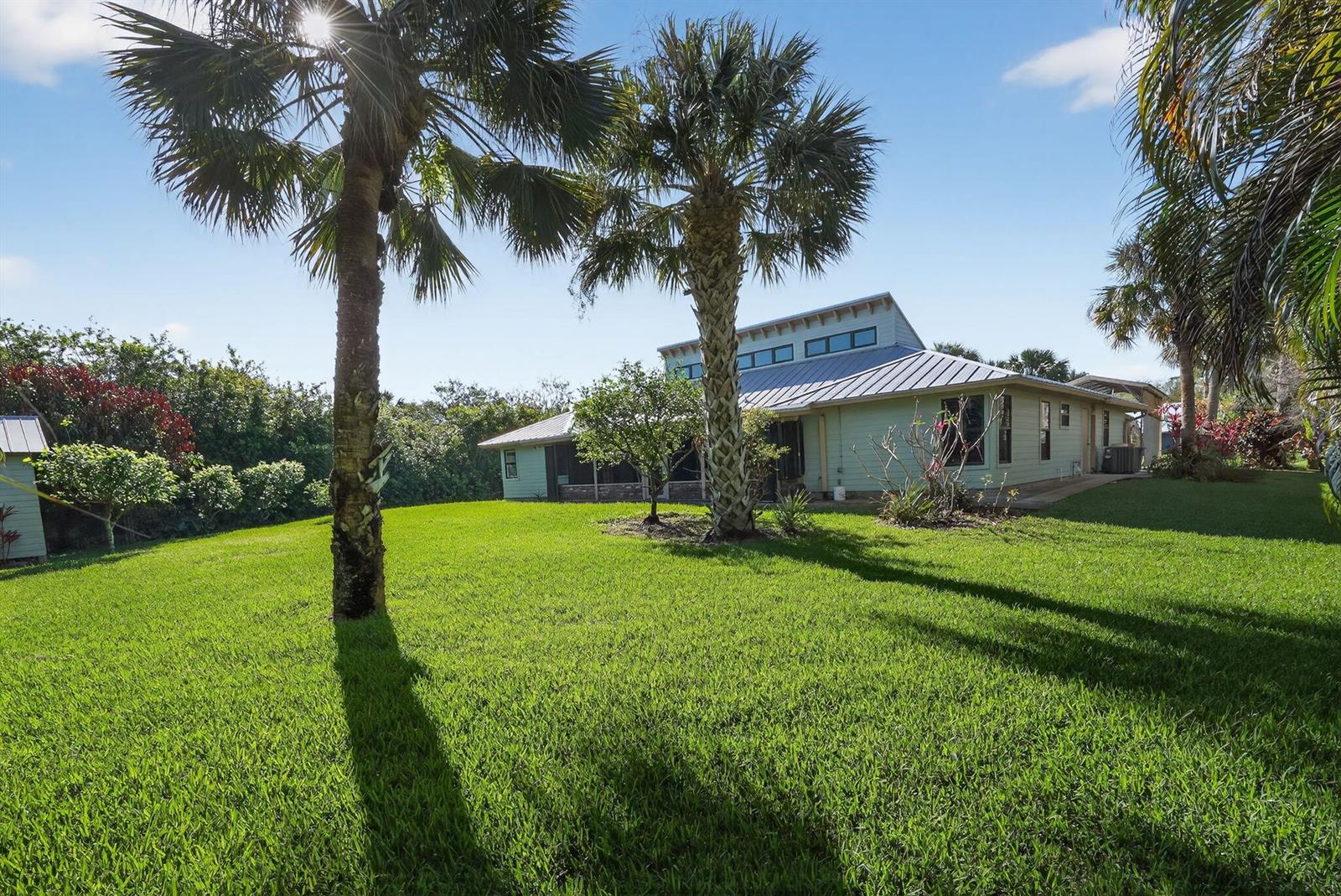 A light green house with a metal roof sits on a grassy lawn with palms — 8535 SE May Terrace, Hobe Sound FL 33455, HOBE SOUND, FL