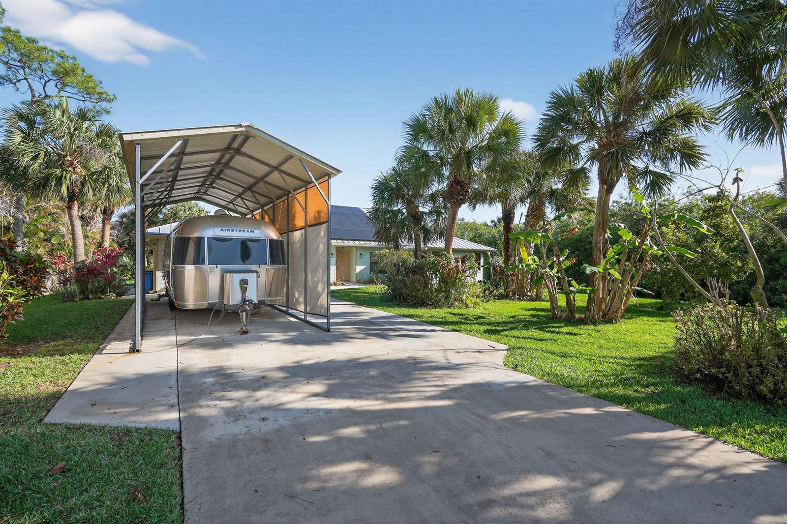 An Airstream trailer is parked under a metal carport next to a house and palm trees — 8535 SE May Terrace, Hobe Sound FL 33455, HOBE SOUND, FL