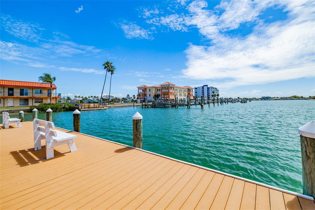 A wooden dock with white benches overlooks a calm bay with buildings and boat slips — 10355 PARADISE BOULEVARD UNIT 511, TREASURE ISLAND, FL