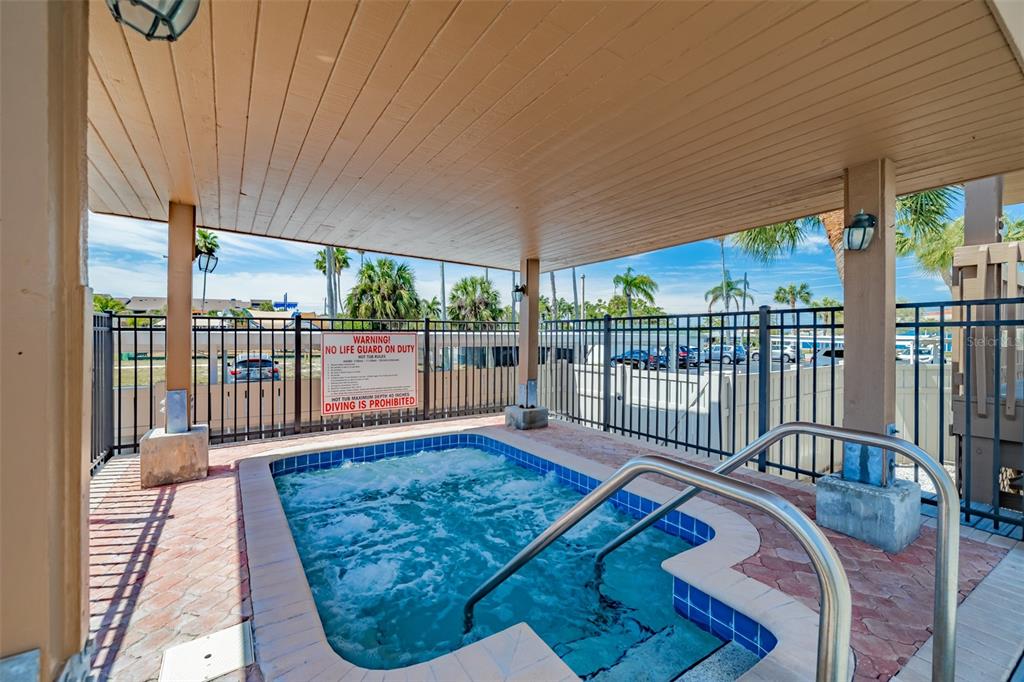 A covered outdoor hot tub with a metal fence and a warning sign — 10355 PARADISE BOULEVARD UNIT 511, TREASURE ISLAND, FL