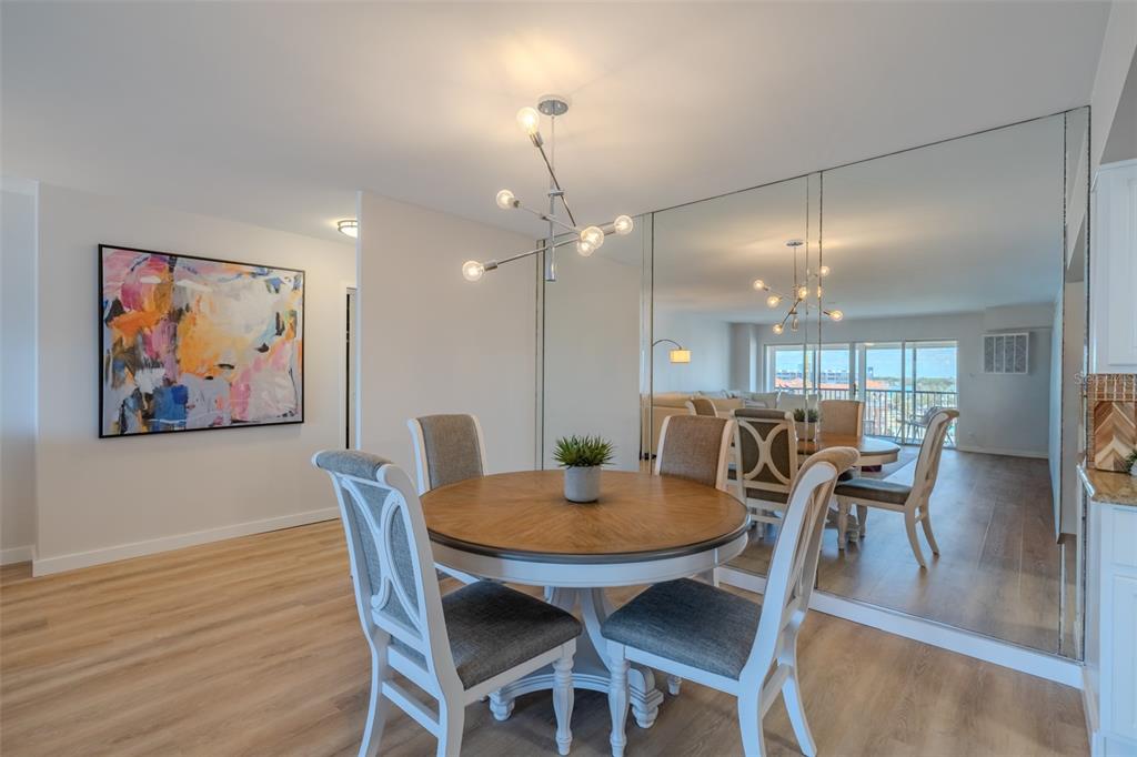 A dining area features a round wooden table, four chairs, and a large mirrored wall — 10355 PARADISE BOULEVARD UNIT 511, TREASURE ISLAND, FL