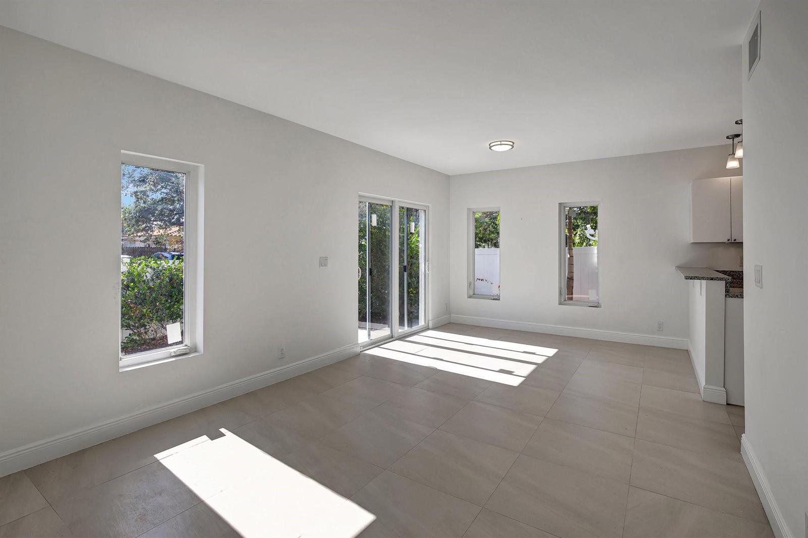 An empty room with white walls, large floor tiles, sliding glass doors, and two windows — 1104 S 20th Avenue, Hollywood FL 33020, HOLLYWOOD, FL