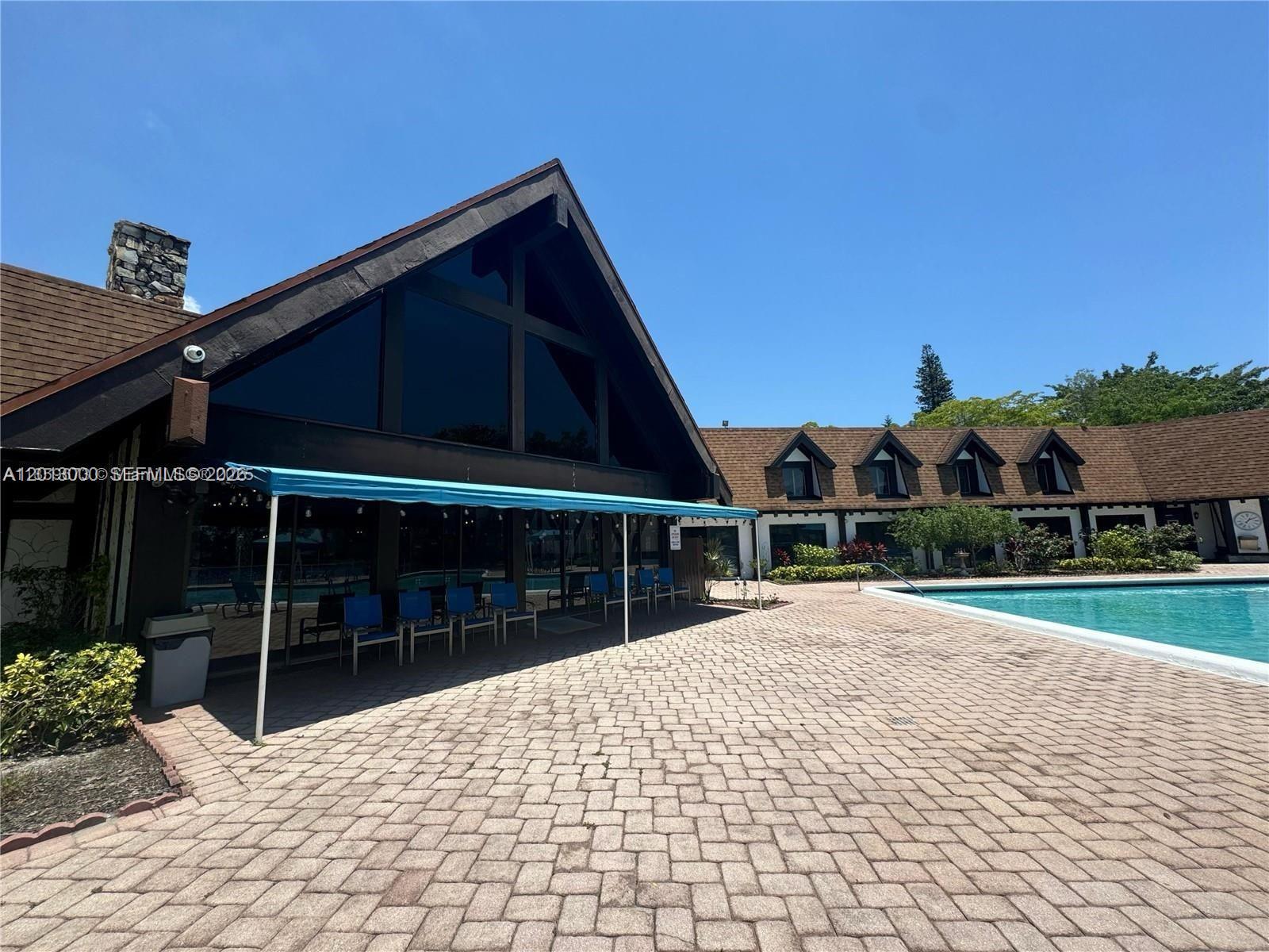 A large A-frame building with a patio and pool sits under a clear blue sky — 3730 Inverrary Dr # 3B, Lauderhill FL 33319, LAUDERHILL, FL