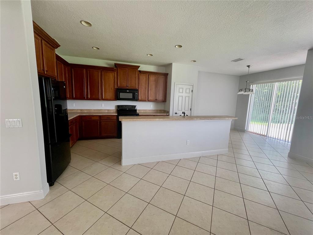 A kitchen with wood cabinets, black appliances, a breakfast bar, and tile flooring — 14257 LAGOON COVE LANE, WINTER GARDEN, FL