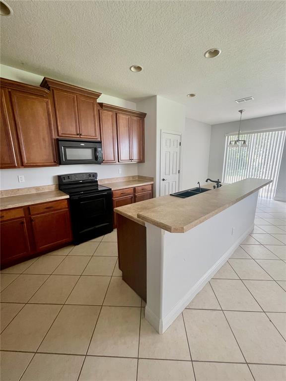 A kitchen features wood cabinets, black appliances, a breakfast bar, and beige tile flooring — 14257 LAGOON COVE LANE, WINTER GARDEN, FL