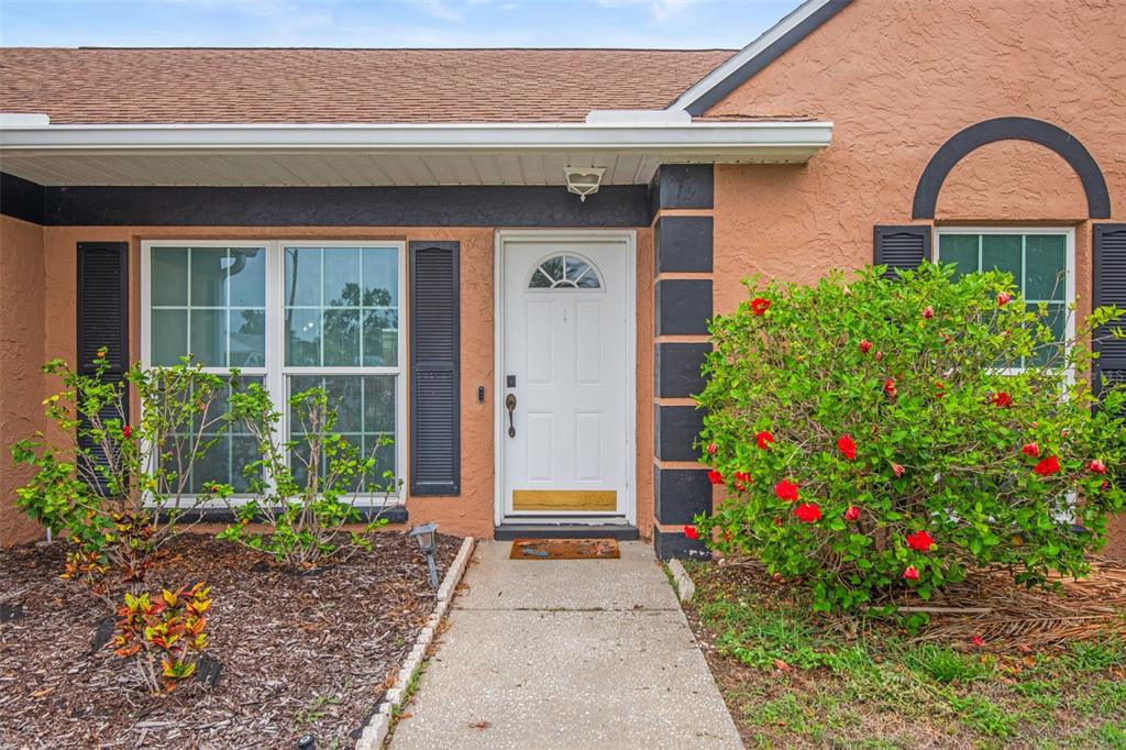 The exterior of a peach-colored house features a white front door, dark shutters, and landscaping — 7591 121ST TERRACE, LARGO, FL