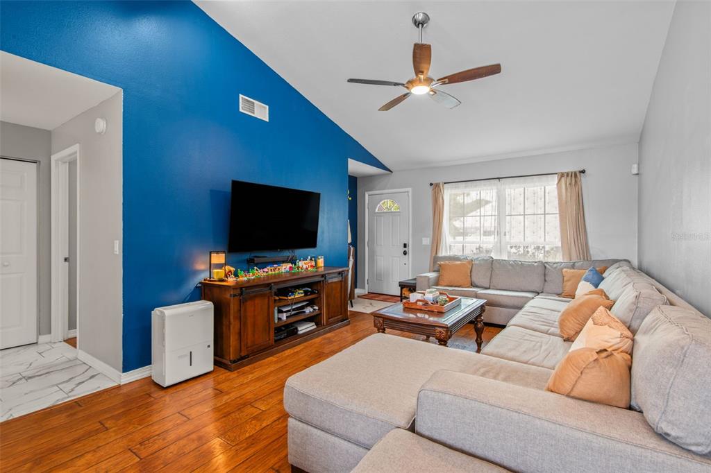A living room features a blue accent wall, a large sectional sofa, and wood flooring — 7591 121ST TERRACE, LARGO, FL