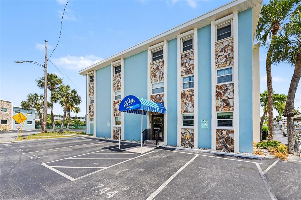 The exterior of a blue multi-story building features a striped awning over the office entrance — 6161 GULF WINDS DRIVE UNIT 153, ST PETE BEACH, FL
