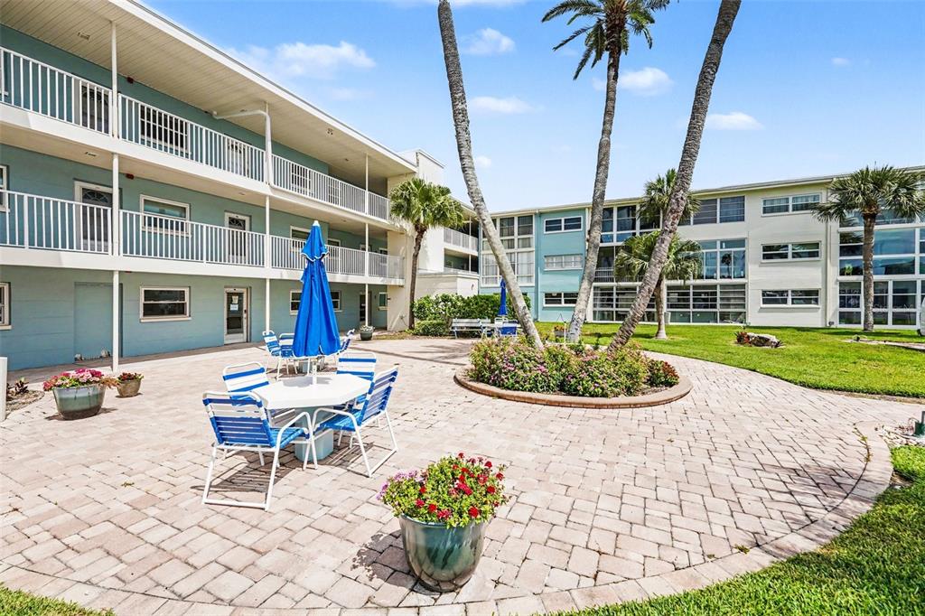 A paved courtyard with a patio table, chairs, and palm trees sits between apartment buildings — 6161 GULF WINDS DRIVE UNIT 153, ST PETE BEACH, FL