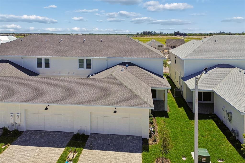 An aerial view shows the exterior of white townhomes with gray shingled roofs and driveways — 8111 SEAFLOWER PARKWAY, BRADENTON, FL