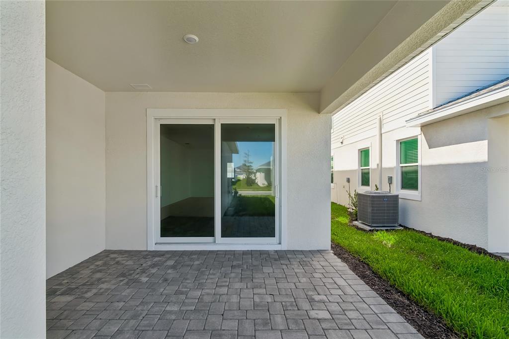 A covered patio features gray paver flooring and a sliding glass door leading indoors — 8111 SEAFLOWER PARKWAY, BRADENTON, FL