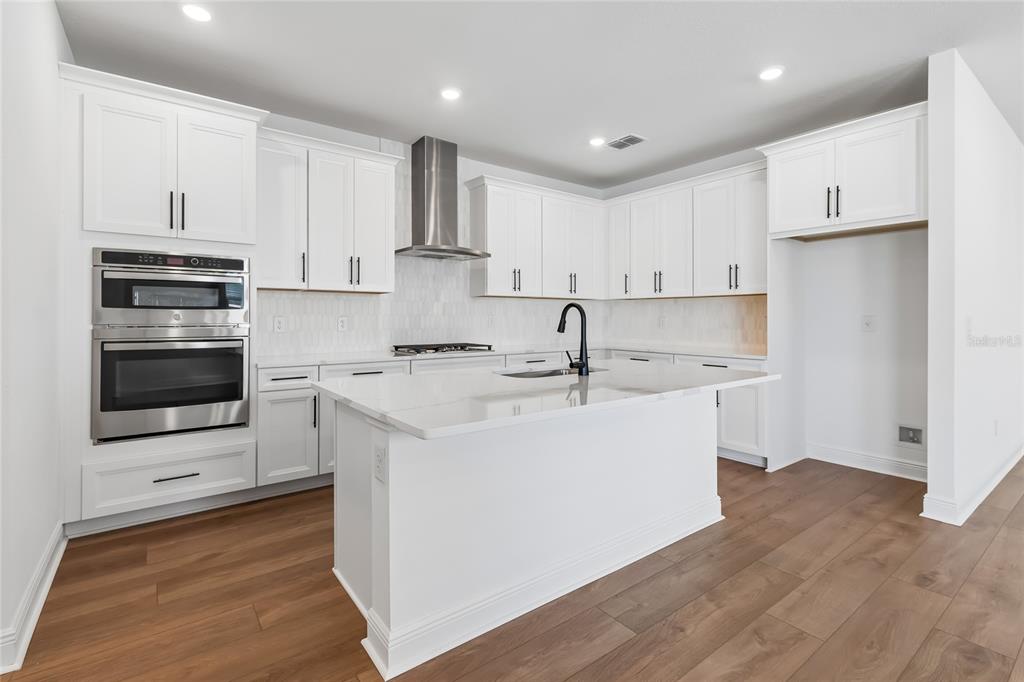 A modern kitchen features white cabinets, stainless steel appliances, a center island, and wood flooring — 8111 SEAFLOWER PARKWAY, BRADENTON, FL