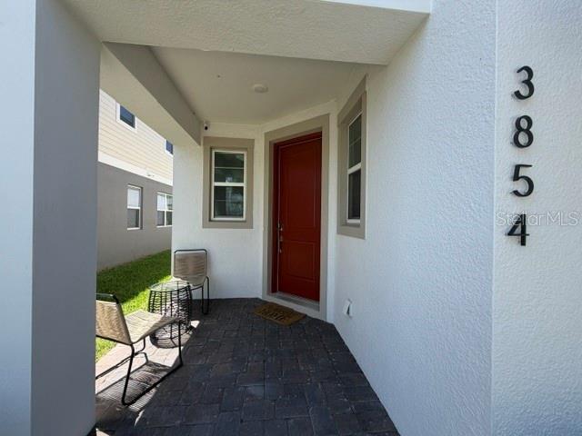 A covered entryway features a red front door, stone flooring, and two outdoor chairs — 3854 KNOTTY PINE STREET, ST CLOUD, FL
