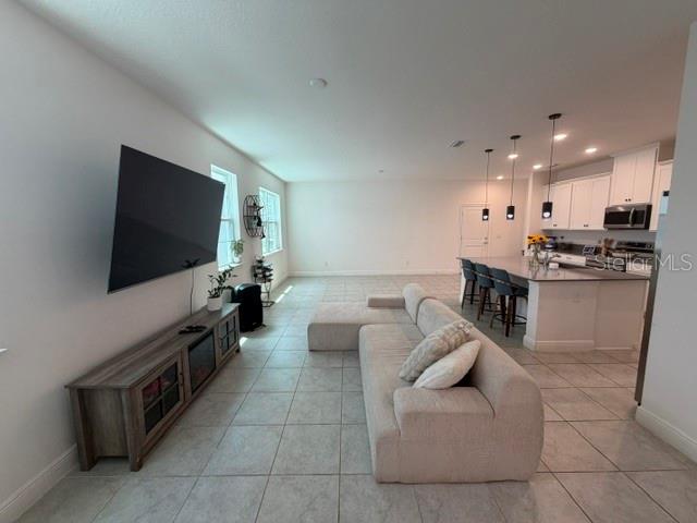A living room with a large television, media console, and sectional sofa opens to a kitchen — 3854 KNOTTY PINE STREET, ST CLOUD, FL