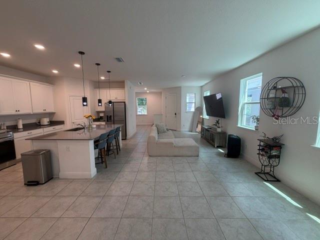 An open-concept kitchen and living area features white cabinetry, a large island, and tile flooring — 3854 KNOTTY PINE STREET, ST CLOUD, FL