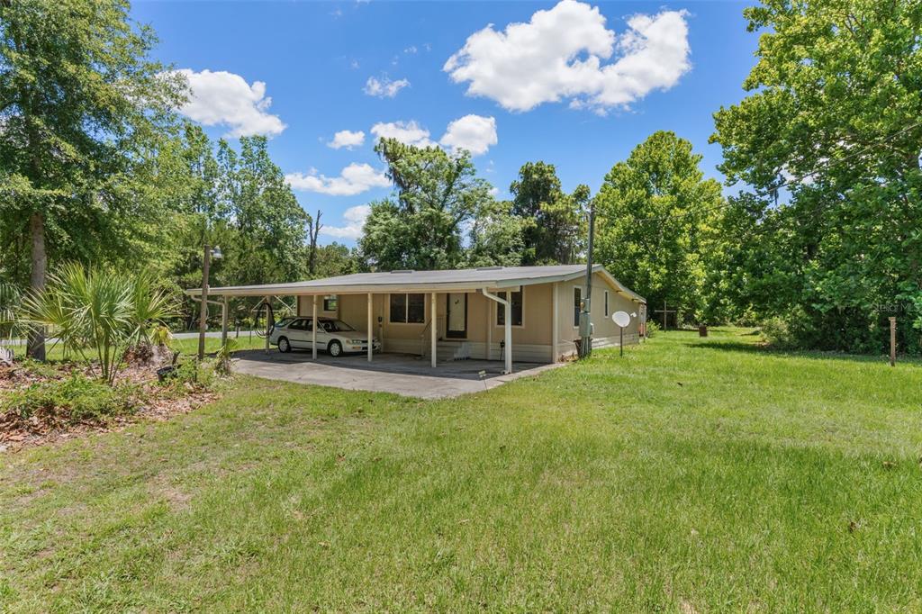 A single-story house with a large carport and a grassy yard under a blue sky — 3909 S CEDAR TERRACE, HOMOSASSA, FL