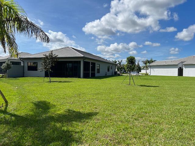 A view of the grassy backyard and rear exterior of a single-story suburban house — 9741 Spruce Woods Drive, Boynton Beach FL 33473, BOYNTON BEACH, FL