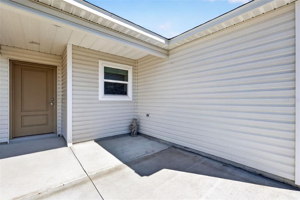 A beige vinyl-sided exterior features a concrete patio, a single window, and a tan door — 7478 SAVANNA DRIVE, THE VILLAGES, FL