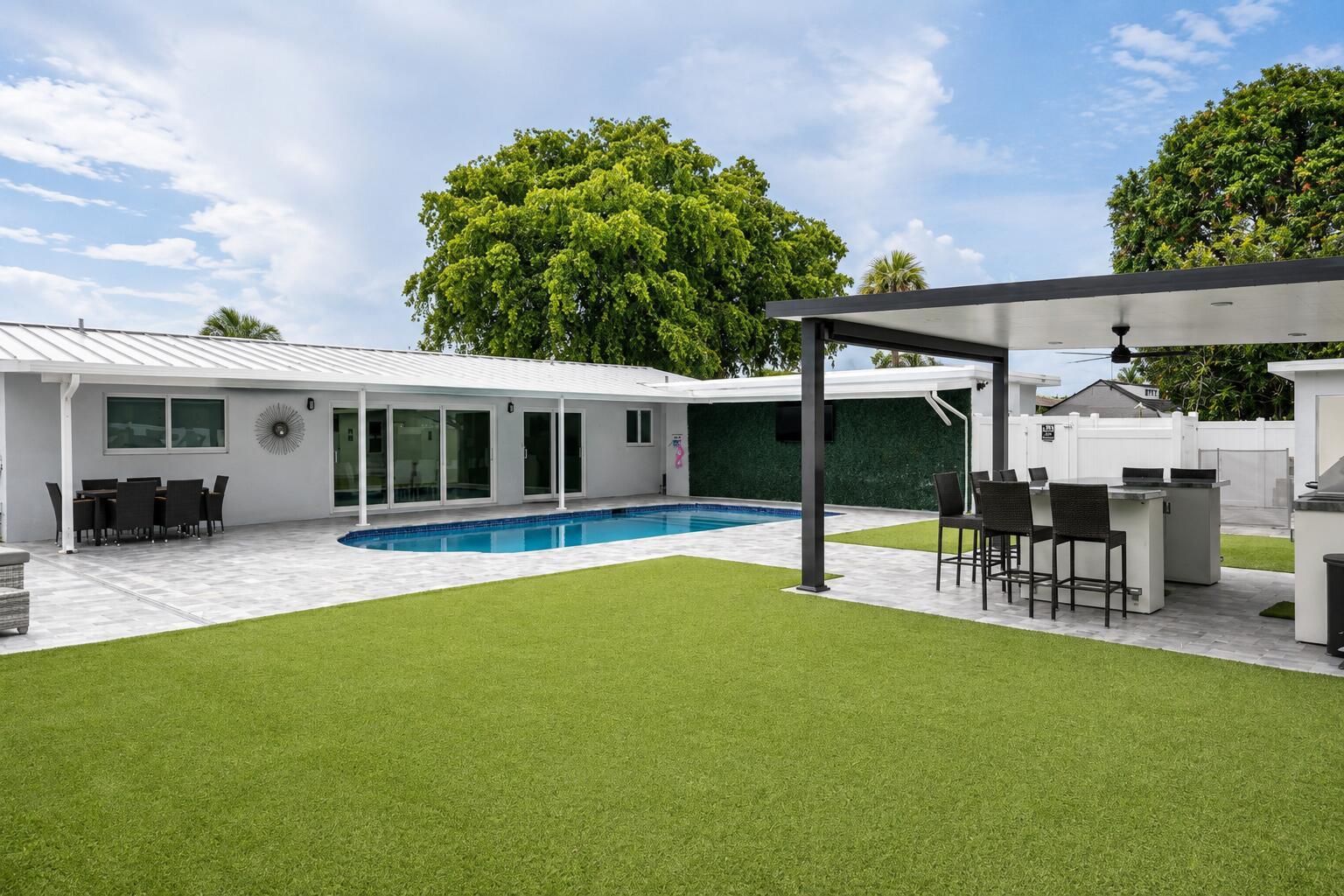 A backyard features a swimming pool, artificial turf, a covered patio, and an outdoor kitchen — 1316 SE 3rd Avenue, Deerfield Beach FL 33441, DEERFIELD BEACH, FL