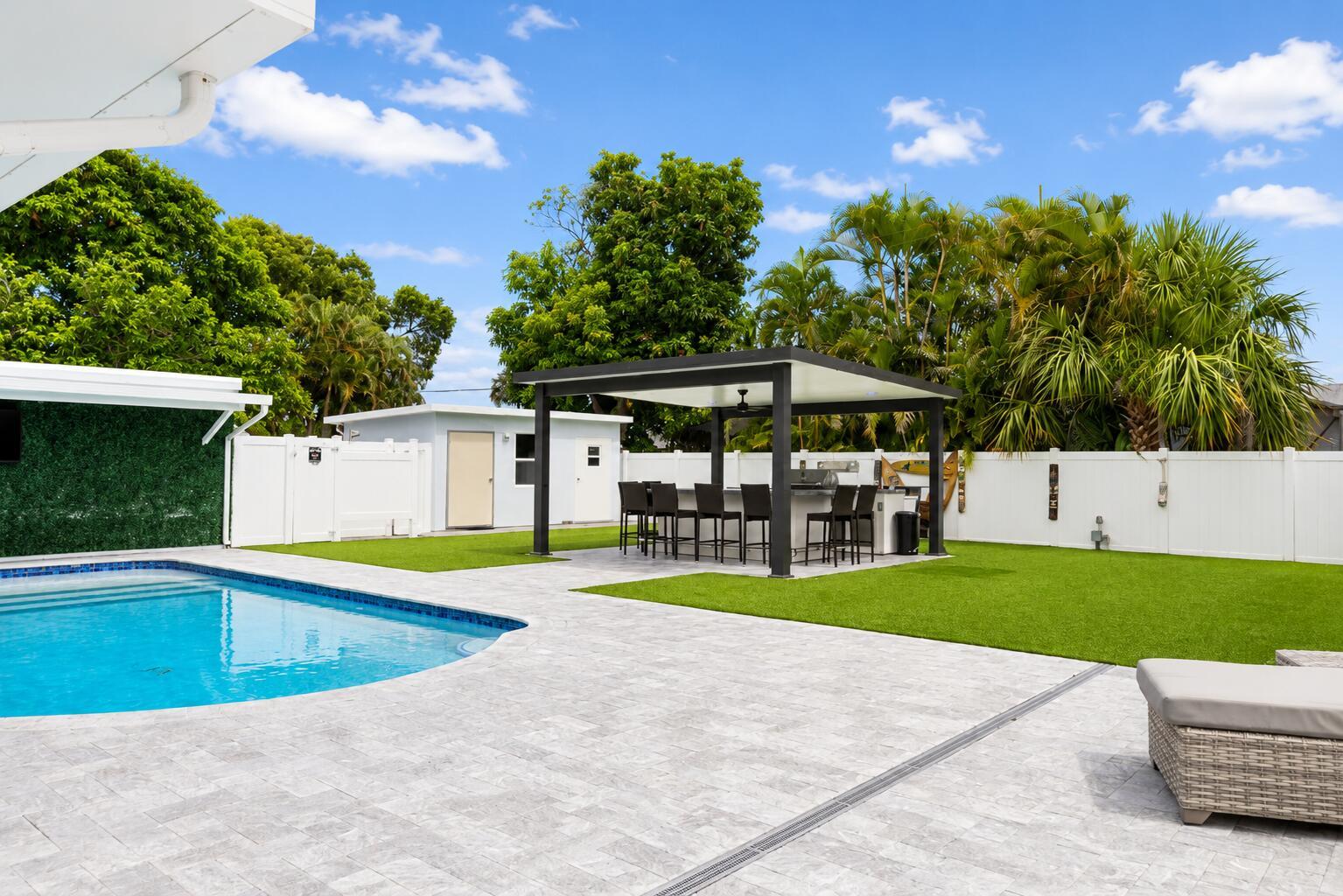 A backyard features a swimming pool, a covered outdoor kitchen, and a white privacy fence — 1316 SE 3rd Avenue, Deerfield Beach FL 33441, DEERFIELD BEACH, FL