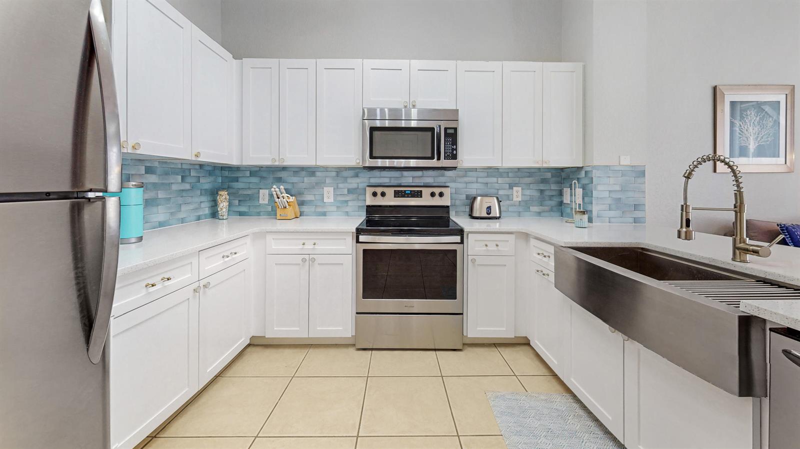A kitchen features white cabinets, stainless steel appliances, a farmhouse sink, and blue tile backsplash — KISSIMMEE, FL