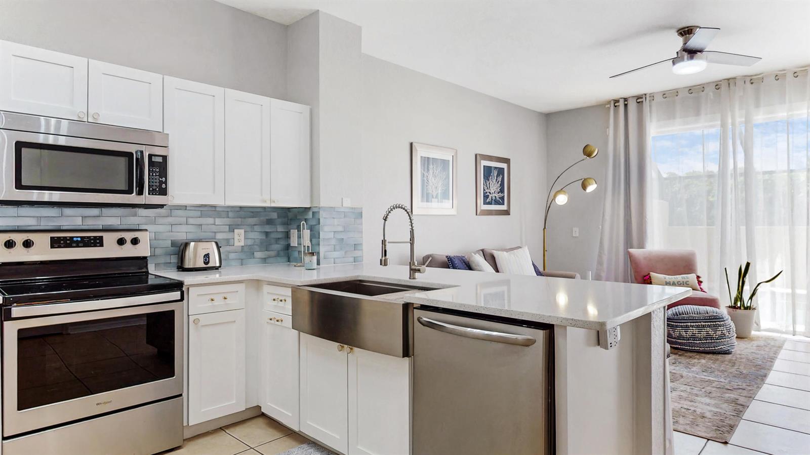 A kitchen with white cabinets, stainless steel appliances, and a farmhouse sink overlooks a living area — KISSIMMEE, FL