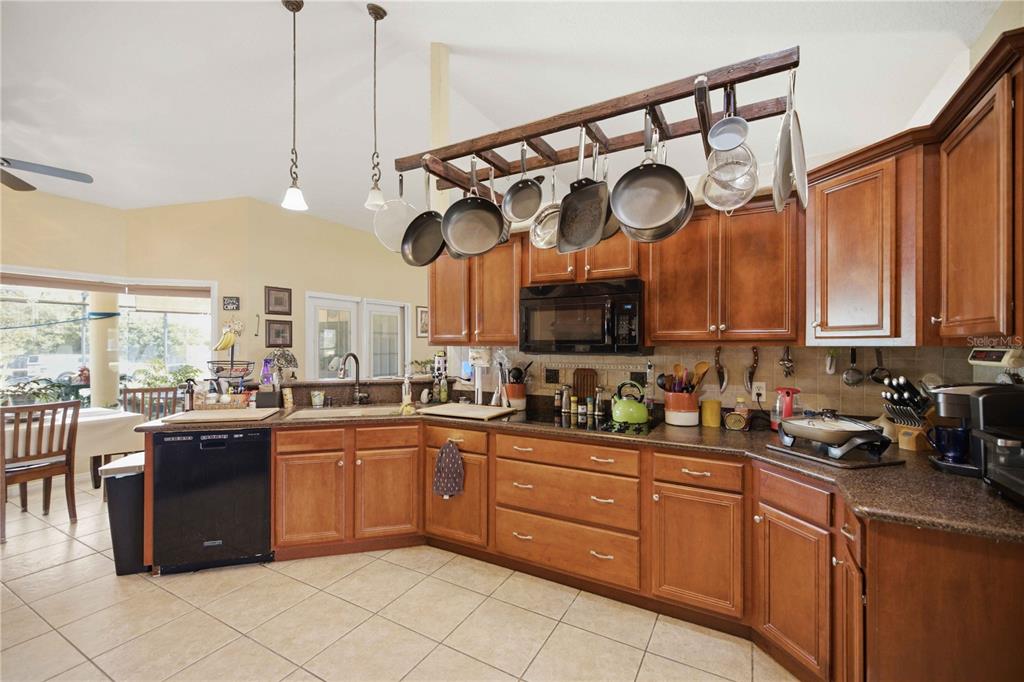 A kitchen features wood cabinets, a hanging pot rack, and a black dishwasher — 4505 SW 106TH PLACE, OCALA, FL