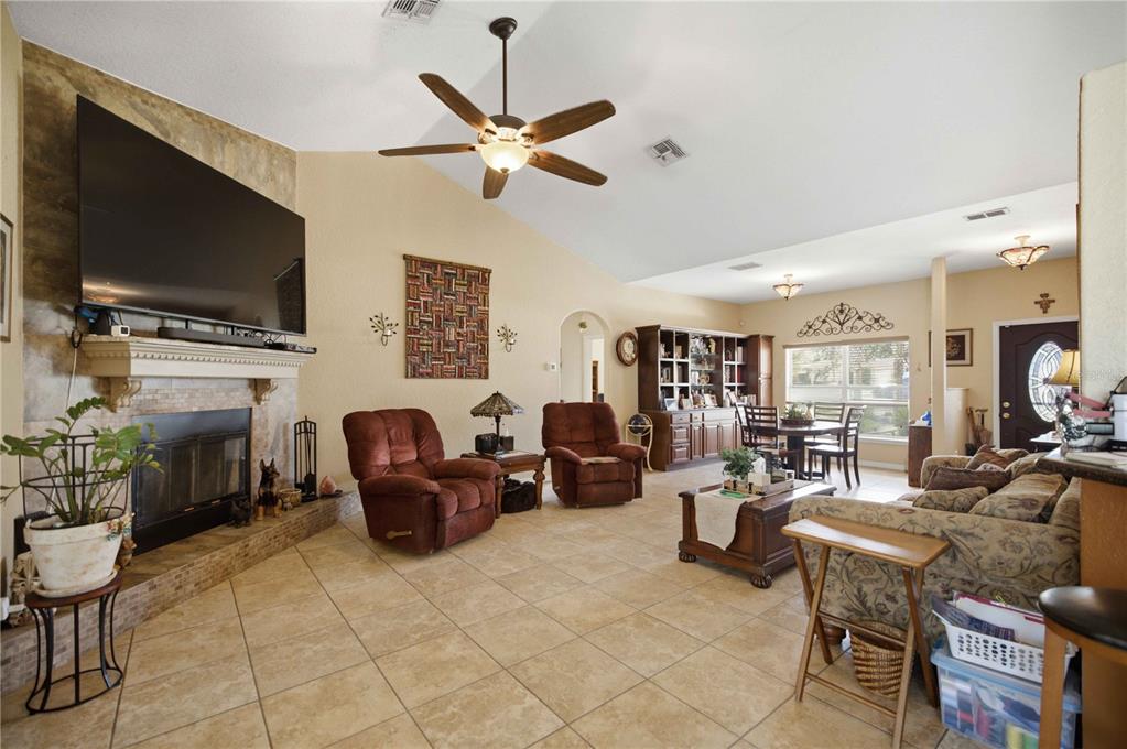 A living room with tile floors, a stone fireplace, a ceiling fan, and dining area — 4505 SW 106TH PLACE, OCALA, FL